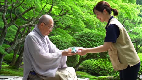 a serene moment in a tranquil garden: an elder monk receiving a thoughtful gift from a young woman amidst lush greenery and peaceful surroundings