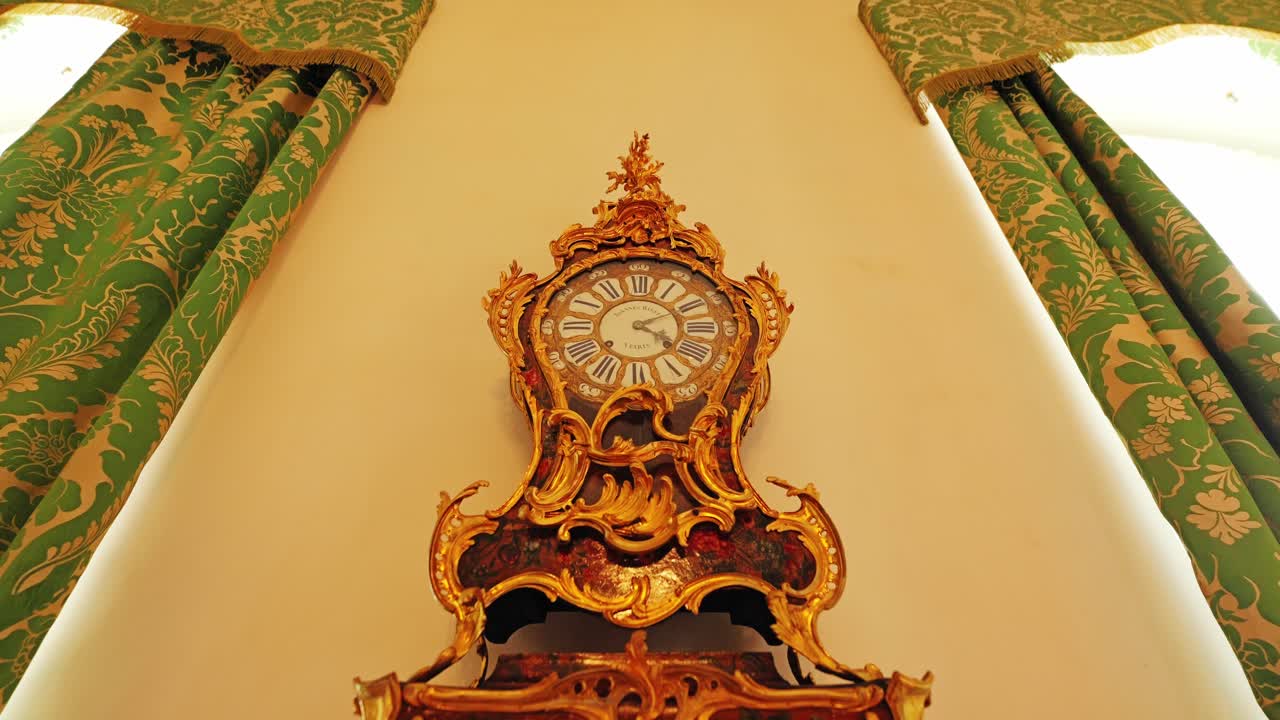Low angle tilt reveals ornate gilded clock framed by patterned palace drapes