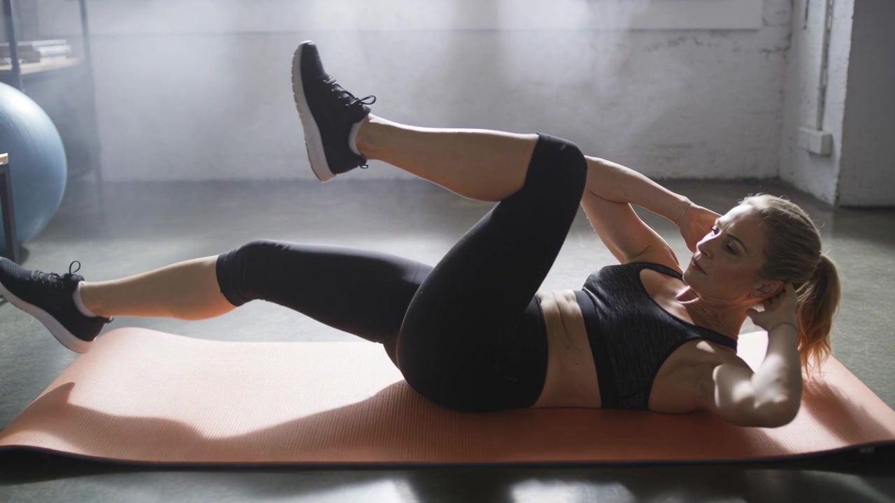 Una donna in abbigliamento sportivo nero esegue crunch a bicicletta su un tappetino arancione per rafforzare il core, con spazio per il testo.