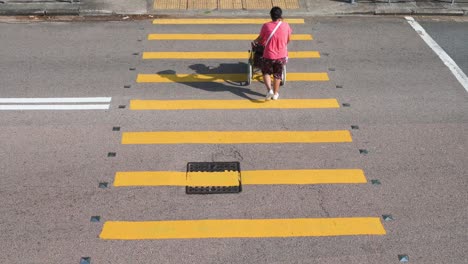 Young-woman-pushing-senior-man-on-a-wheelchair-as-they-go-through-a-zebra-crossing-while-male-pedestrian,-behind-them,-walks-across-as-well-in-Hong-Kong