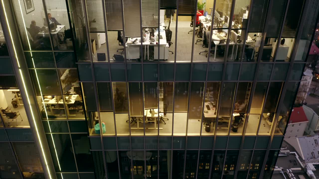 Vista aérea de un rascacielos nocturno con ventanas de oficina y gente de negocios trabajando hasta tarde en computadoras