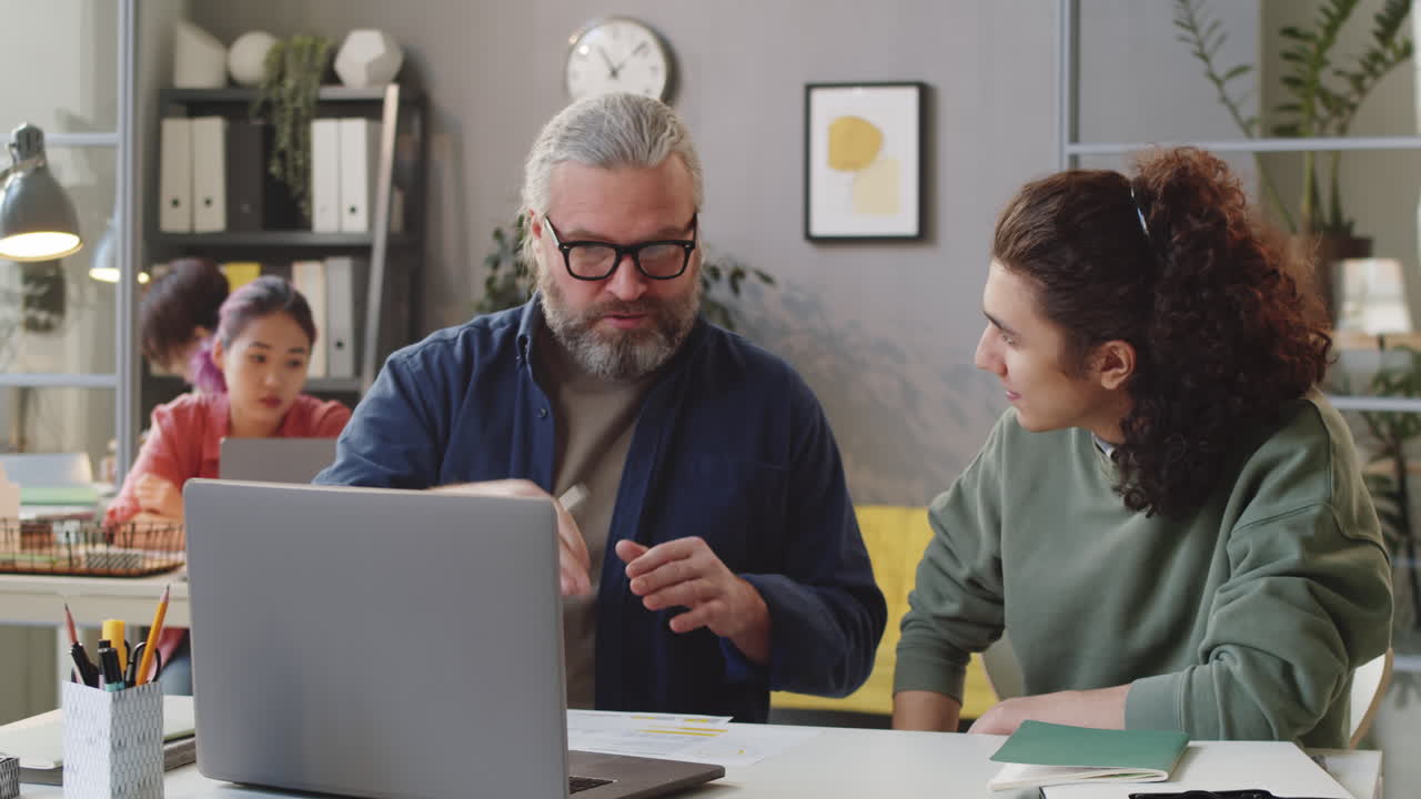 mentor sénior y joven aprendiz discutiendo el proyecto en la computadora portátil