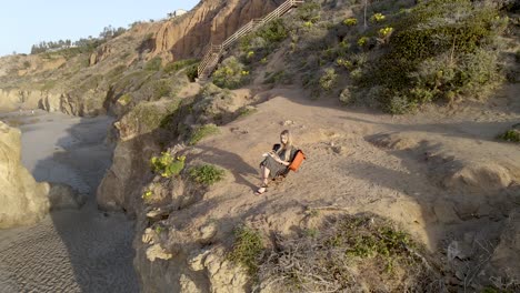 young woman reading a book on cliff top above el matador beach, malibu