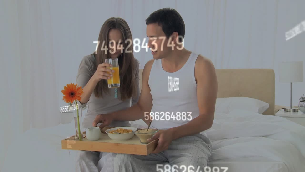Man bringing tray, placing on lap, woman sipping, sharing lifestyle breakfast under numeric overlay