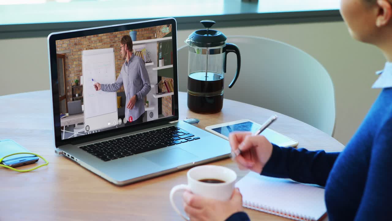Kaukasisk kvindelig studerende bruger bærbar computer på videoopkald med mandlig lærer og tager noter.