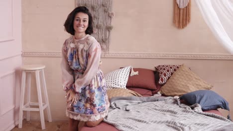 Cheerful-happy-young-brunette-girl-with-short-hair,-wearing-beautiful-dress,-jumping-or-falling-on-comfy-bed.-Indoors-footage