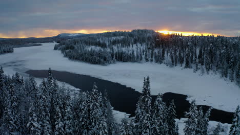 beautiful aerial view orbiting left across snowy lapland sweden winter lake landscape forest trees at sunrise