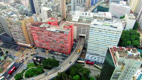 Traffic-passing-through-a-Car-park-building-in-downtown-Hong-Kong,-with-city-mega-buildings,-Aerial-view