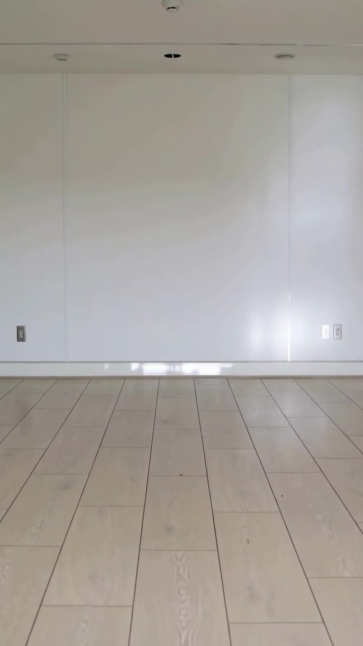 Video vertical: Mostrando la pared de un estudio, suelo de madera recibiendo el sol de una ventana a la derecha, enchufes visibles