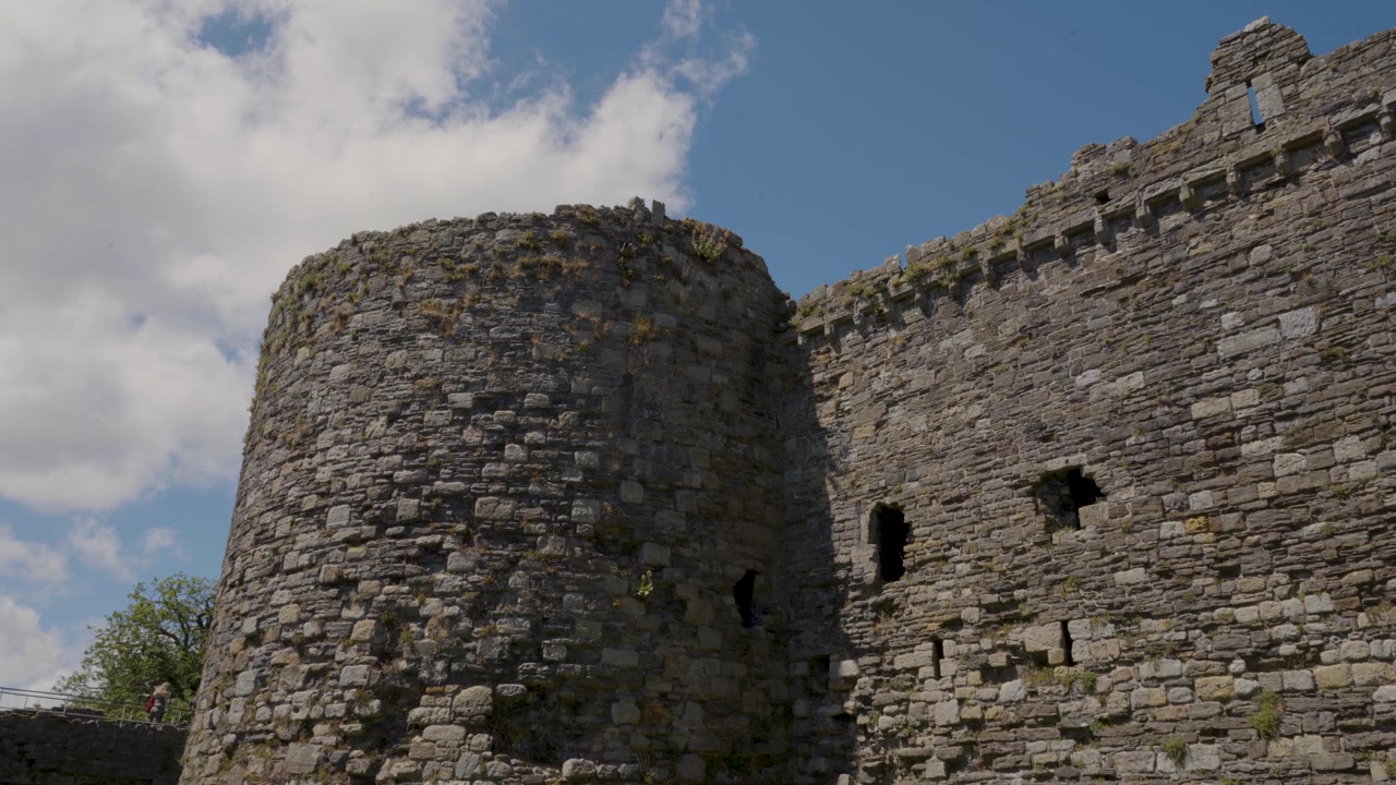 Inquadratura statica del Castello di Beaumaris che si concentra sulle mura in pietra medievali e sulle imponenti torri, rivelando muratura dettagliata, texture invecchiate e caratteristiche architettoniche storiche.