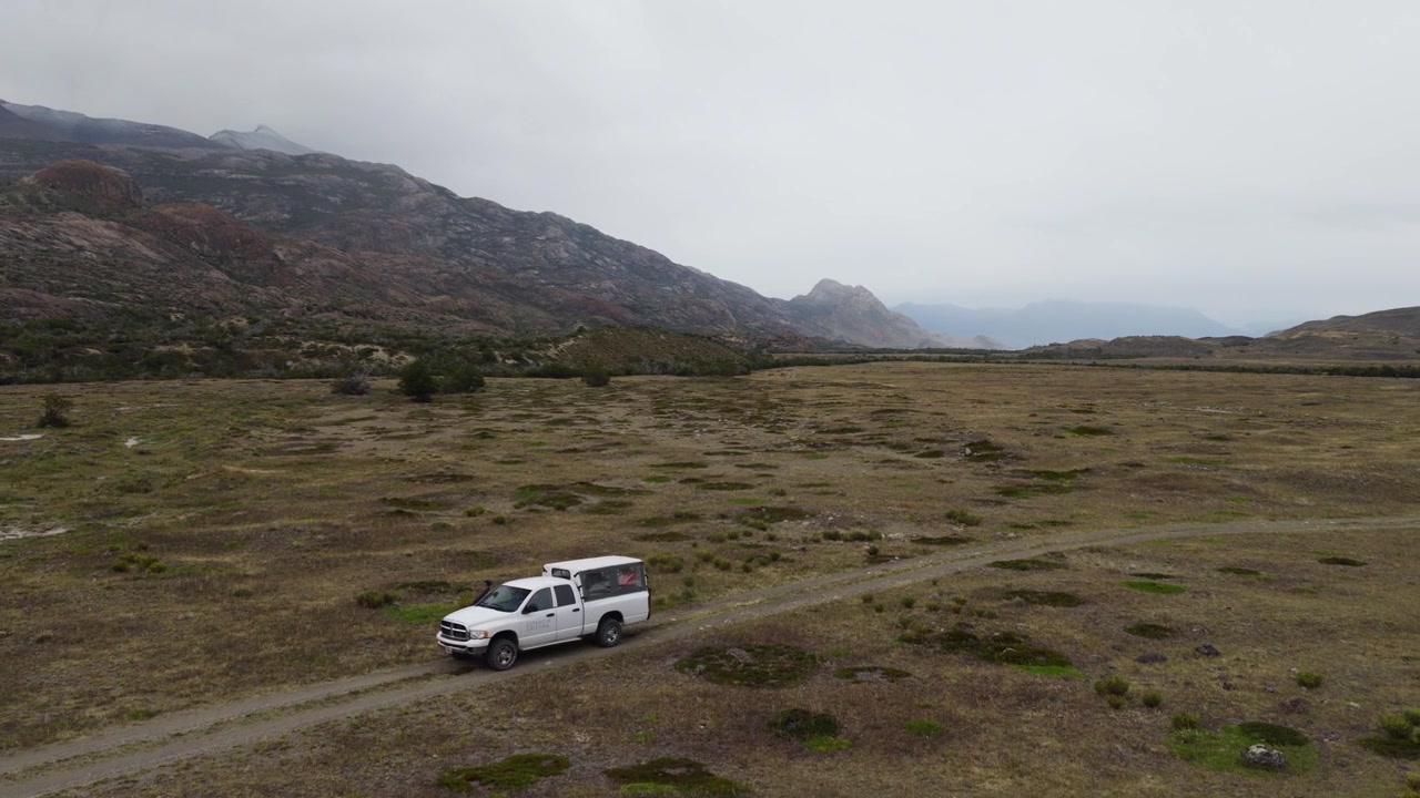 Caminhonete de expedição a conduzir por estepe remota perto de El Chaltén, Santa Cruz, Patagônia, Argentina, rodeada por contrafortes rochosos dos Andes, vegetação arbustiva esparsa e paisagens de vales glaciais.