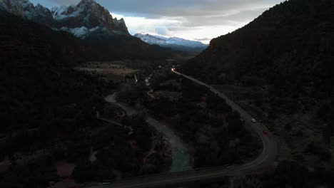 aerial pan up shot following 2 cars as they pass through a stunning red rock mountain valley during sunset.