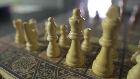 trucking shot from left to right of old white chess pieces standing on a chessboard with blur background at home