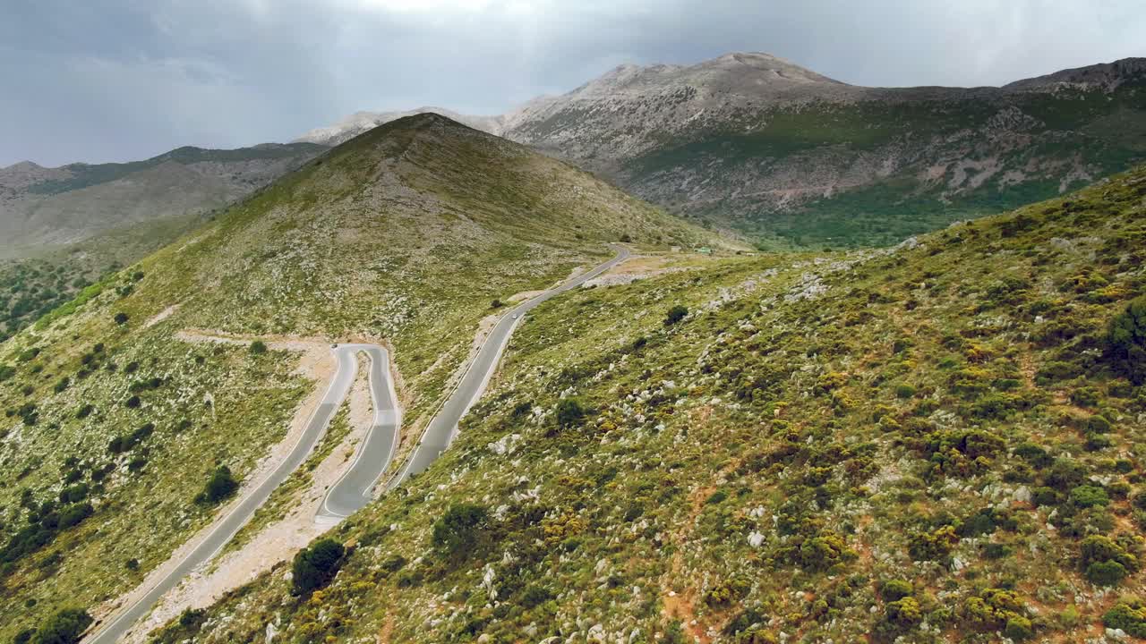 impresionante vista aérea de pequeñas carreteras con curvas en majestuosas montañas enormes, bajo el cielo nublado