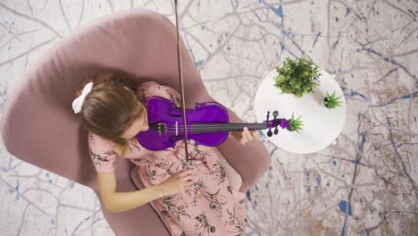 musician woman sitting on sofa at home and playing violin.