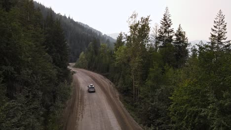 silver car driving into a vast boreal forest in british columbia that is covered with smoke from wildfires