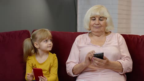 Senior-grandmother-with-child-girl-granddaughter-using-digital-mobile-phone,-playing-games-at-home