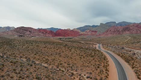 Toma-Aérea-De-Un-Dron-De-Una-Carretera-Desértica-Vacía-Con-Pintorescas-Montañas-Al-Fondo