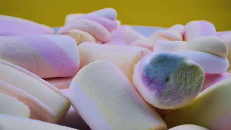 a lot of whole sweet pastel marshmallows, spinning on a yellow background