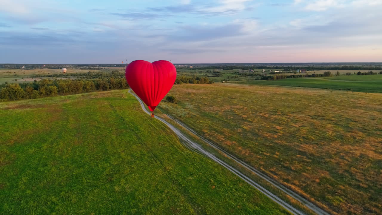 Travel of romantic hot air balloon. Red aerostat balloon flying over the fields under blue sky. Beautiful aerostat in the form of a heart.Aerial view.