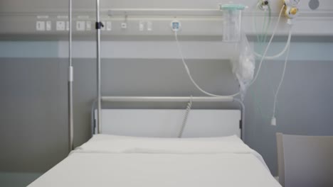 Rack-focus-shot-of-empty-hospital-bed-with-drip-and-stands-in-hospital-ward,-slow-motion