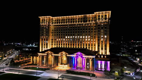 aerial orbit shot in front of the night lit michigan central station in detroit