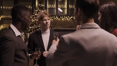 group friends wearing stylish clothes while talking and holding champagne glasses at new year's party 1