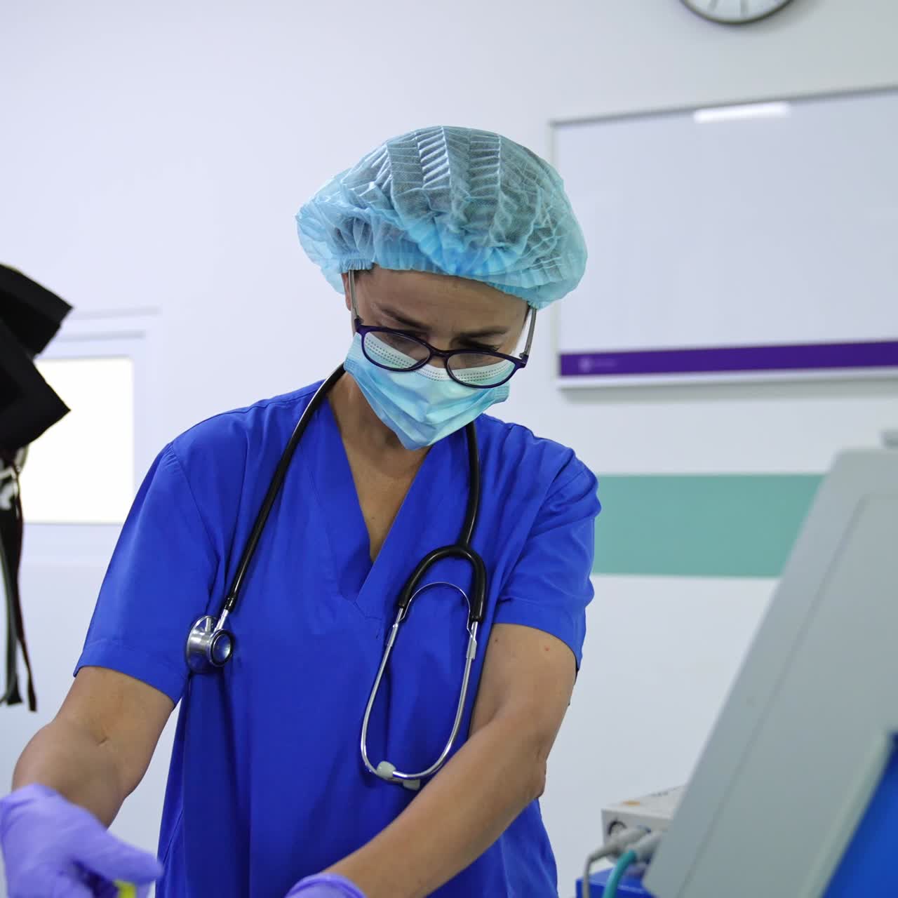 Female doctor anesthesiologist gives a shot to a patient. Medic wearing glasses and stethoscope on her shoulders looks at equipment