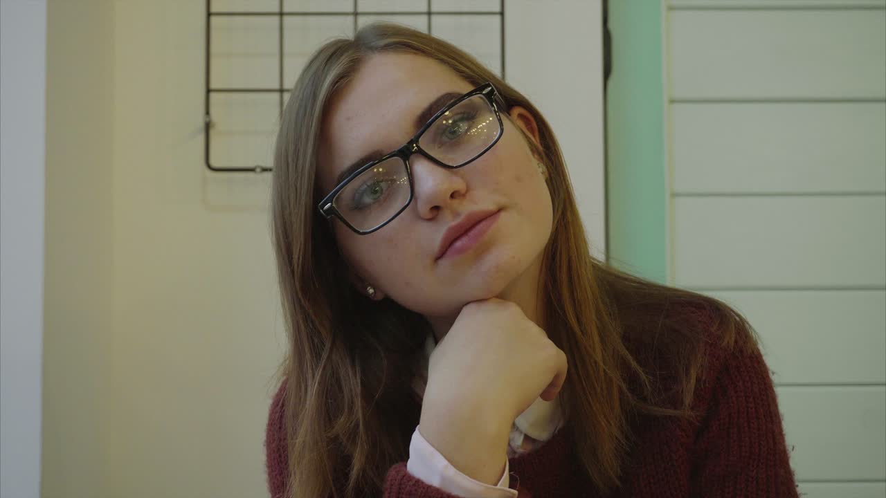 una mujer con gafas, en un café, mirando pensativa.