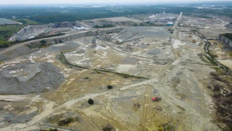 aerial drone revelaing and flying backwards over and above a large wet mining quarry where limestone gravel and building materials are being made with heavy equipment during day, gravel mountains seen