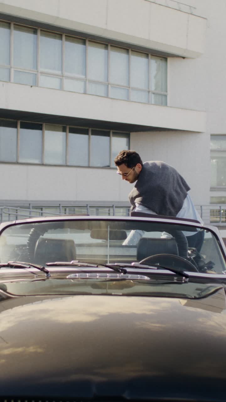 People in a classic convertible car in front of a building