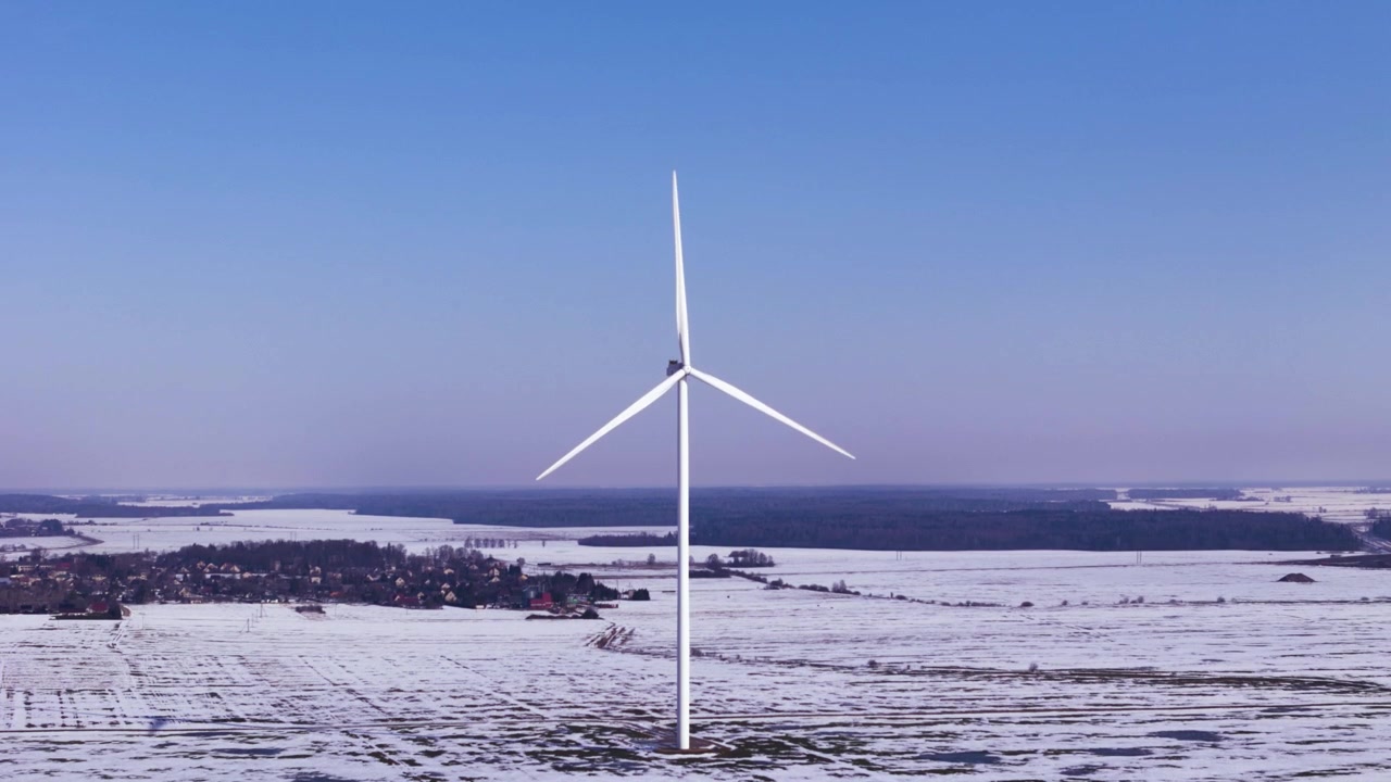 Vindmølle står i et vidt, snedækket landskab under en klar blå himmel.