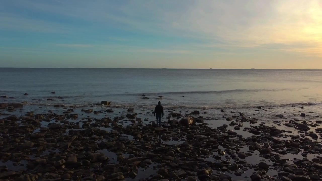 Följeskott av en man som går över en klapperstensstrand en kväll, County Durham