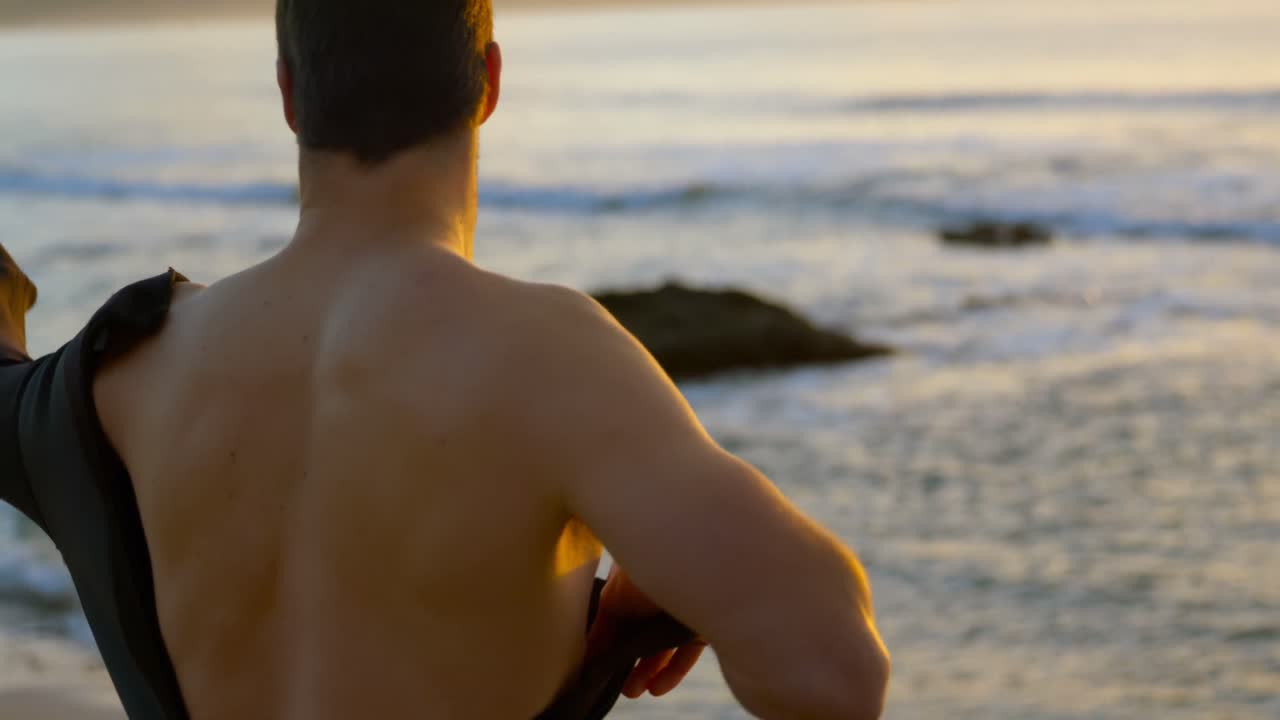 해가 지는 동안 해변에서 서핑복을 입은 중간 성인 백인 남자의 측면 뷰 4k