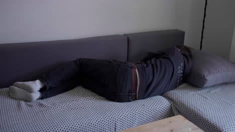 young man lying on the couch sleeping and waking up in living room wearing black hoodie and black pants