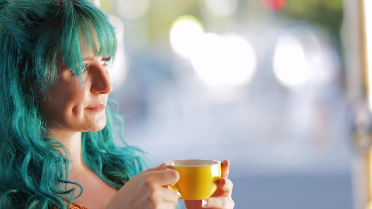 atractiva mujer milenaria con cabello azul bebiendo de una taza amarilla, espacio de copia bokeh
