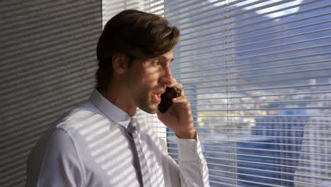 Side-view-of-young-Caucasian-male-executive-talking-on-mobile-phone-near-window-in-modern-office-4k