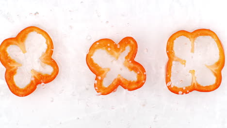 slow motion water splash on three slices of pepper lying on a white background in water