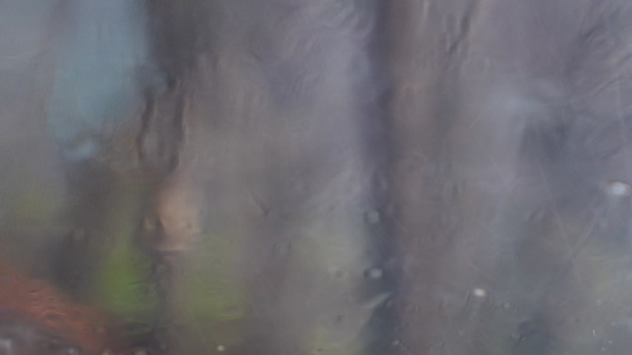 Rain drops on window glass of a car with the blurry scene of the trees