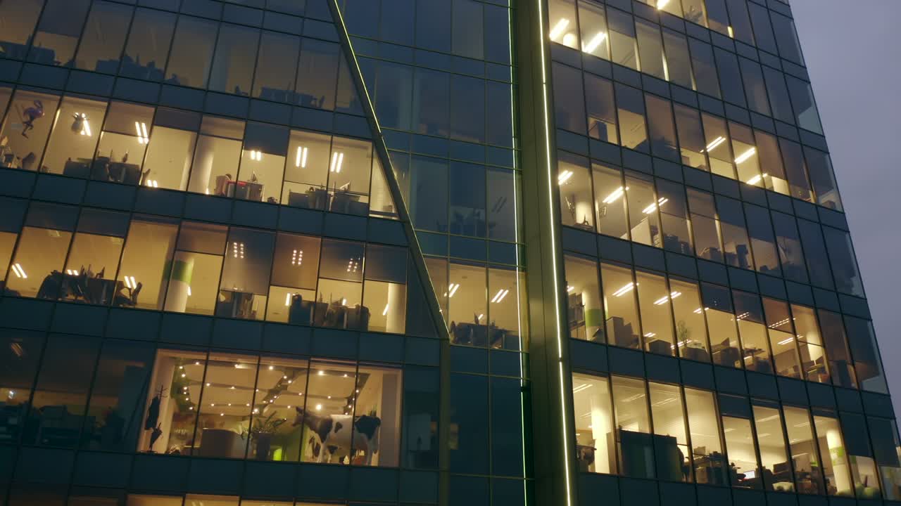 vista cinematográfica desde un dron de un rascacielos nocturno con ventanas de oficinas y personas de negocios trabajando en computadoras tarde en la noche.