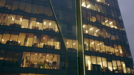 cinematic view from a drone of a night skyscraper with office windows and business people working at computers late at night.