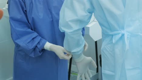 nurse helping to surgeon to put protective gloves on before operation.