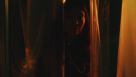 portrait of asian girl behind plastic wrap curtains in colorful neon light