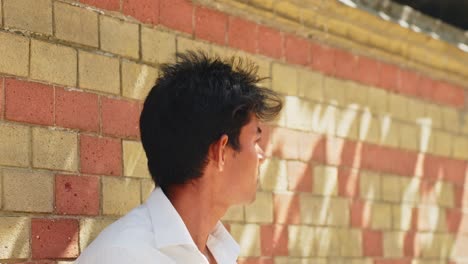 asian male model with short black hair and white shirt posing against brick wall