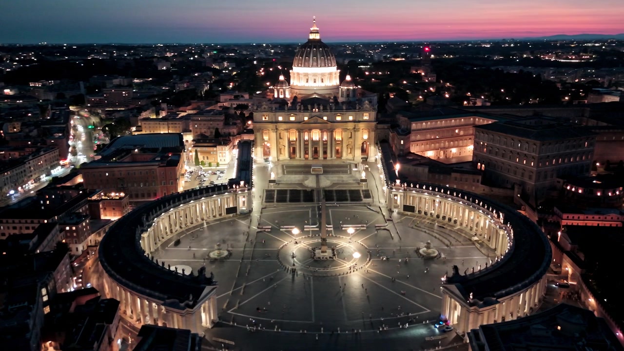 La Basílica de San Pedro y la elíptica Plaza de San Pedro brillan a la hora azul mientras un dron avanza lentamente sobre la Ciudad del Vaticano.