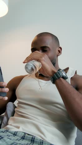 man relaxing at home, drinking water and using phone