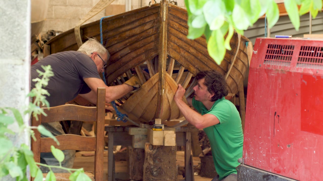 Reparando un barco de madera tradicional de tingladillo, un joven aprendiz y un carpintero de ribera.
