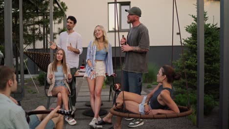 a group of friends relax and sing while their friend plays the guitar in the courtyard of a country house during vacation