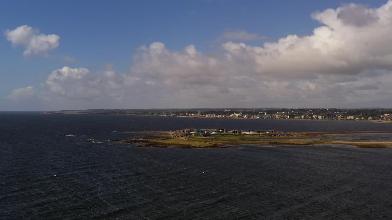aproximación aérea de la isla de mutton en la bahía de galway, irlanda, mostrando la costa y el océano circundante bajo un cielo parcialmente nublado
