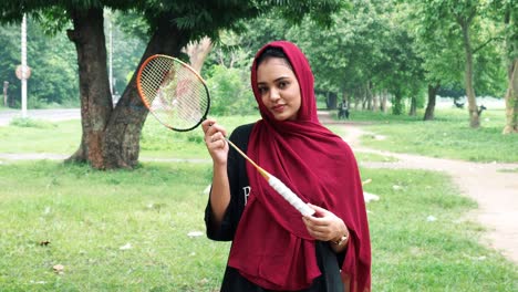 Vista-De-Cerca-De-Una-Hermosa-Chica-Afgana-Con-Hiyab-Sosteniendo-La-Raqueta-De-Bádminton-Sonriendo-Y-Mirando-A-La-Cámara